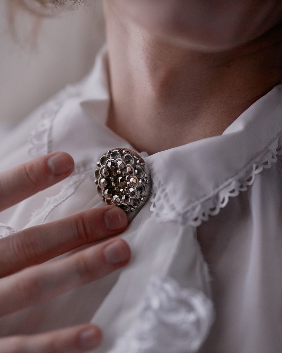 Eine alte Brosche liegt neben einem neu gefertigten Ring auf Leinen